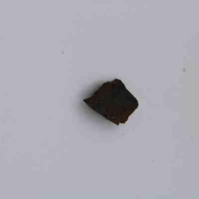 Basaltic glass flake: A small, dark basaltic glass flake is centered against a clean, white background, emphasizing its rough texture and unique geological characteristics.