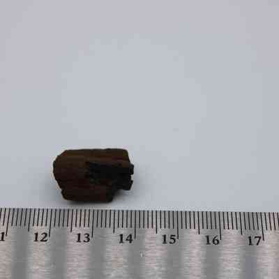 Small core of basaltic glass with ruler: A basaltic glass core, dark and irregular, sits adjacent to a metallic ruler, highlighting its small size and unique texture.