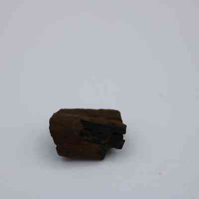 Closeup of basaltic glass core: The image shows a small, dark basaltic glass core with a rough, irregular texture, lying on a plain, light-colored background.