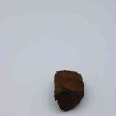 Closeup of basaltic glass core: The image shows a piece of basaltic glass core, displaying its rugged, earthy brown surface on a plain backdrop.