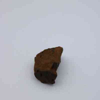 Small basaltic glass core closeup: The image shows a small piece of basaltic glass core with a rough, uneven surface and a dark, earthy brown color.