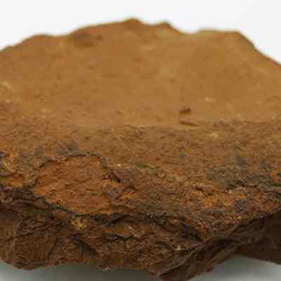 Close up profile of a grinding stone: The image shows a rough, brown grinding stone with an uneven, textured surface, used historically for grinding grains or other materials in various cultural practices.