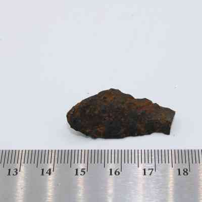 Basaltic glass piece with ruler: The image shows a piece of basaltic glass with a rough texture placed beside a metric ruler on a white background.