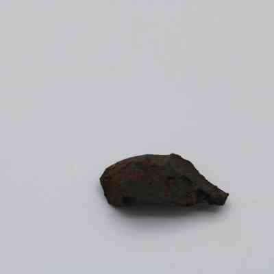 Basaltic glass flake: A small, dark piece of basaltic glass flake rests against a plain, light background, displaying a rugged and irregular surface.