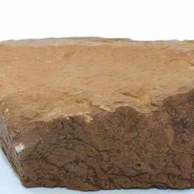 Profile of grindstone: The image depicts a large, irregularly shaped grinding stone with a rough surface, likely used for traditional grinding or sharpening tasks, resting on a light background.