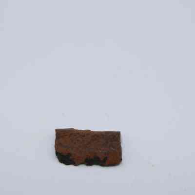 Closeup of tiny basaltic glass core: The image shows a small piece of basaltic glass core with a rough, mottled surface resting against a plain, white background.