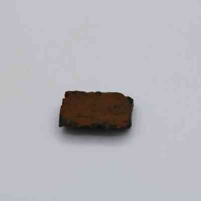 Closeup of basaltic glass core: The image shows a small rectangular piece of basaltic glass core placed on a plain white surface, highlighting its dark, rugged texture.