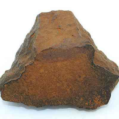 End of a whetstone (hoana) fragment: The image shows a rough, triangular-shaped fragment of a whetstone with a brown, weathered surface and visible texture, possibly used historically for sharpening.
