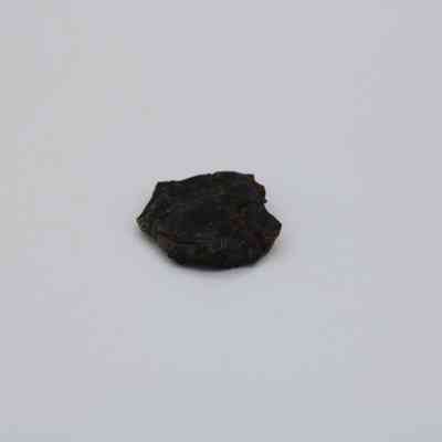 Closeup of basaltic glass flake: A small, dark basaltic glass flake sits isolated on a plain white background, showcasing its rough texture and irregular shape.