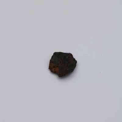 Closeup of basaltic glass flake: The image shows a small, irregularly shaped flake of basaltic glass resting against a plain white background.