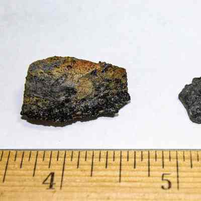 Closeup of two pieces of volcanic glass: The image shows two dark, textured rock samples placed on a plain surface, with a ruler indicating their size.