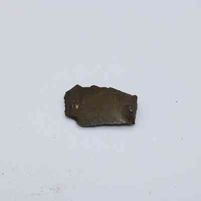 Closeup of basaltic glass flake: A small, dark flake of basaltic glass rests on a plain, light background, highlighting its rough texture and edges.