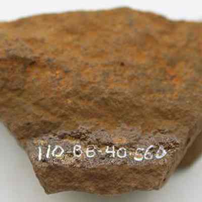 Whetstone (hoana) fragment with alternate id number visible: The image shows a rough, brown fragment of a whetstone (hoana), with a series of white numbers and letters, "110-BB-40.560."