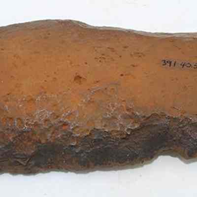 Basalt knife (pahi) with alternate id number visible: The image depicts a roughly shaped knife (pahi) made from a piece of brown stone, with rugged edges and a textured surface.