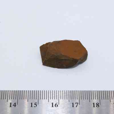 Closeup of basaltic glass piece and ruler: The image shows a small, roughly shaped piece of basaltic glass placed against a white background, with a measurement ruler below indicating its size.