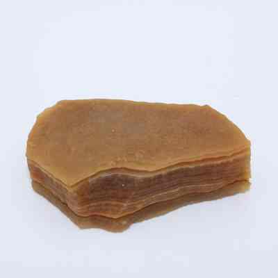Closeup of agate flake: A brown agate flake lies on a white background, displaying layered, translucent bands with an uneven edge.