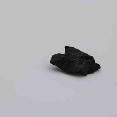 Profile of a basaltic glass cortex flake: The image displays a dark basaltic glass flake with a rough texture, placed against a plain, neutral background.