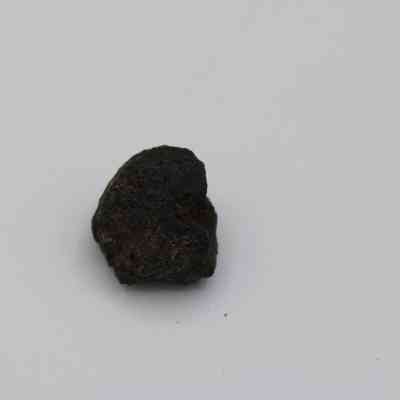 Closeup of basaltic glass core: The image shows a small, irregularly shaped piece of basaltic glass core, dark in color against a plain white background.