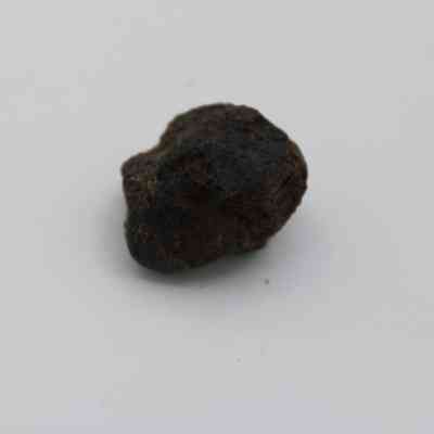 Closeup of basaltic glass core: The image shows a small, rough-textured black basaltic glass core placed against a neutral white background.