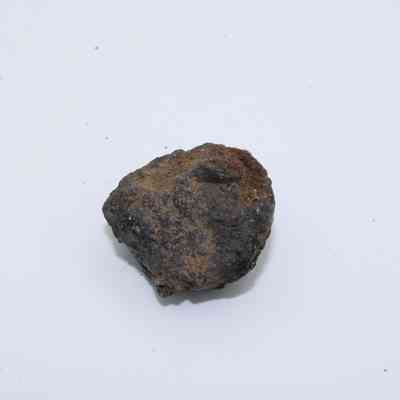 Closup of basaltic glass core: A small piece of basaltic glass core rests on a plain white surface, showcasing a rough texture with dark and earthy tones.