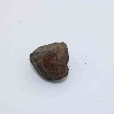 Basaltic glass core: The image shows a small, irregularly shaped piece of basaltic glass core, with a rough, rugged exterior, resting on a plain white surface.