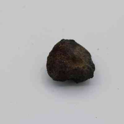 Closeupu of basaltic glass core: The image shows a rough, dark basaltic glass core resting on a smooth, plain white surface, highlighting its texture and irregular shape.