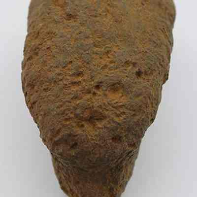 Lenthwise view of breadloaf sinker with ruler: The image shows a rough, brown, bread loaf shaped stone resting on a flat surface, next to a ruler for scale.