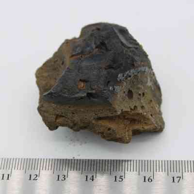 Closeup of basaltic glass core and ruler: This image shows a basaltic glass core displaying dark, glossy textures alongside porous, rough surfaces, placed near a measuring scale.