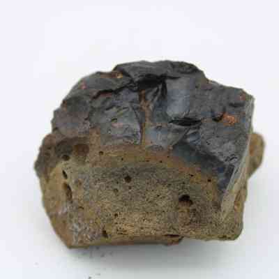 Closeup of side profile of basaltic glass core: The image shows a piece of basaltic glass core featuring a dark, glassy surface atop a porous, rough-textured rock base.