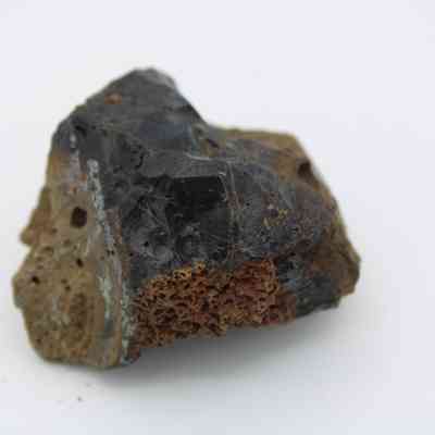 Closeup side profile of basaltic glass core: The image shows a basaltic glass core rock with a smooth, dark surface and a rough, porous reddish-brown section.