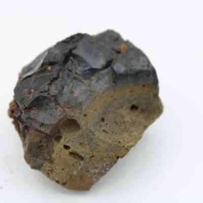 Closeup of basaltic glass core: The image shows a rough basaltic glass core, displaying dark, smooth surfaces and jagged, fractured edges, indicative of its volcanic origin.