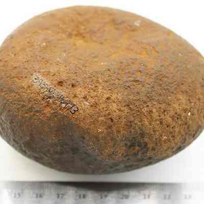 Basalt hammerstone with ruler: The image shows a large, rough, brownish round stone with a ruler below for scale comparison.