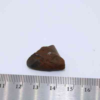 Tiny piece of basaltic glass: A small piece of basaltic glass rests beside a ruler for scale, showcasing its rugged texture and dark color.