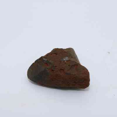 Small piece of basaltic glass: The image shows a piece of basaltic glass, characterized by its dark, rough texture and an earthy coating against a plain, light background.
