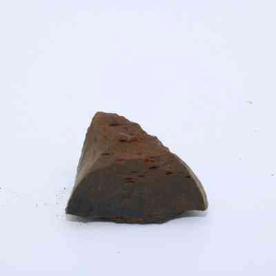 Triangular piece of basaltic glass: The image shows a small, rough-edged piece of basaltic glass with a dark, matte surface, resting on a white background.