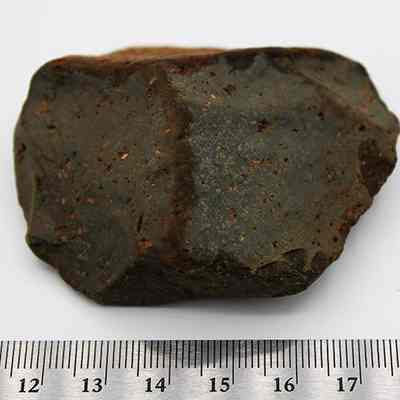Basalt core/scraper with ruler: A dark, irregularly shaped rock is displayed against a white background, accompanied by a ruler featuring centimeter measurements for scale.