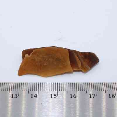 Closeup of calcite and metal ruler: A piece of brown calcite lies on a white surface, accompanied by a ruler showing measurements, highlighting its size.