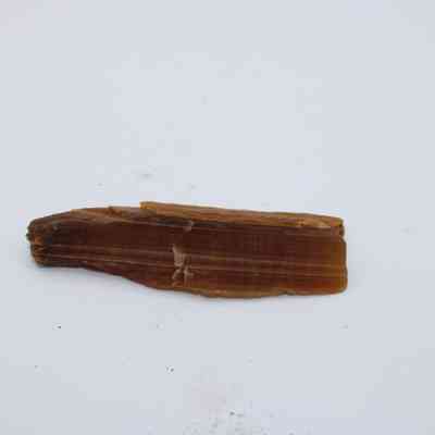 Profile of a calcite piece: A piece of brown calcite lies on a plain white background, showcasing its smooth, elongated shape and natural layered texture.
