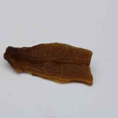 Closeup of calcite piece profile: A brown, irregularly shaped calcite specimen lies on a plain white background, showcasing subtle surface textures and natural earthy tones.