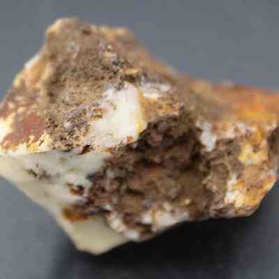 Closeup of quartzite core: The image shows a rough, irregular piece of quartzite with brown earthy material embedded in it, resting against a soft-focus dark background, highlighting its natural texture.