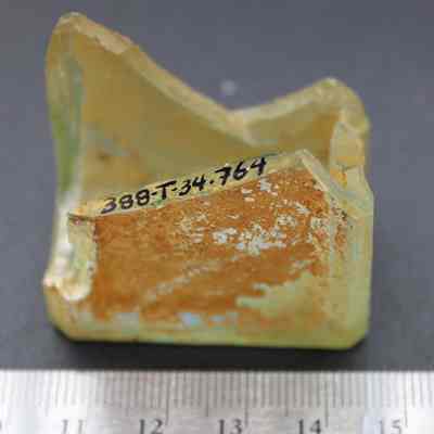 Glass bottle base fragment with ruler: The image shows a weathered bottle fragment with a label "388-T-34.764," displayed on a gray surface beside a ruler measuring approximately 4.5 cm.