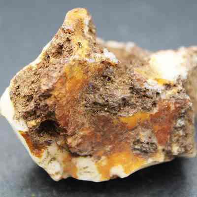 Closeup of quartzite core: The image shows a rough, multicolored mineral rock (probably quartzite) with various shades of brown, orange, and white set against a dark background.