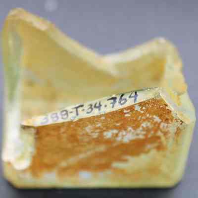 Closeup of glass bottle bottom fragment with alternate id number visible: The image shows a weathered bottle fragment with the inscription "388T34.764" written on one side.