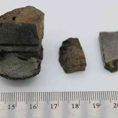 Basaltic glass core with pieces with ruler: The image shows three basaltic glass core fragments, varying in size and texture, next to a metal ruler displaying measurements for scale.