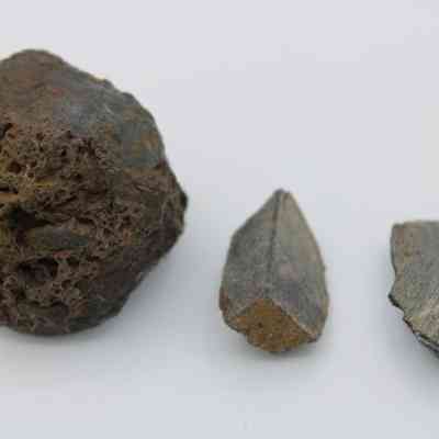 Closeup of basaltic glass core with pieces: The image shows three irregular basaltic glass core pieces on a white background, displaying differing textures and reflective surfaces.