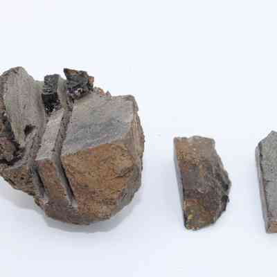 Basaltic glass core with pieces: The image shows a fragmented basaltic glass core with a rough texture, featuring jagged edges and a dark, glassy appearance on a white background.