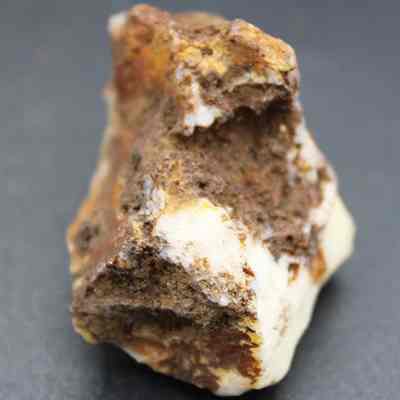 Closeup of quartzite core: The image shows a rough, irregularly shaped rock with a combination of white, brown, and yellow mineral deposits, sitting on a plain dark gray surface.