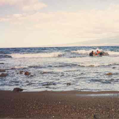 Two people launching another person on a boogie board into the ocean