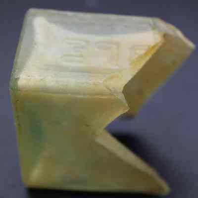Glass bottle fragment closeup: The image shows a jagged, translucent bottle fragment with embossed numbers and a smooth, weathered surface, resting against a dark background.