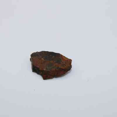 Closeup of basaltic glass flake: A single, dark basaltic glass flake with reddish-brown tones, rests on a plain white surface.